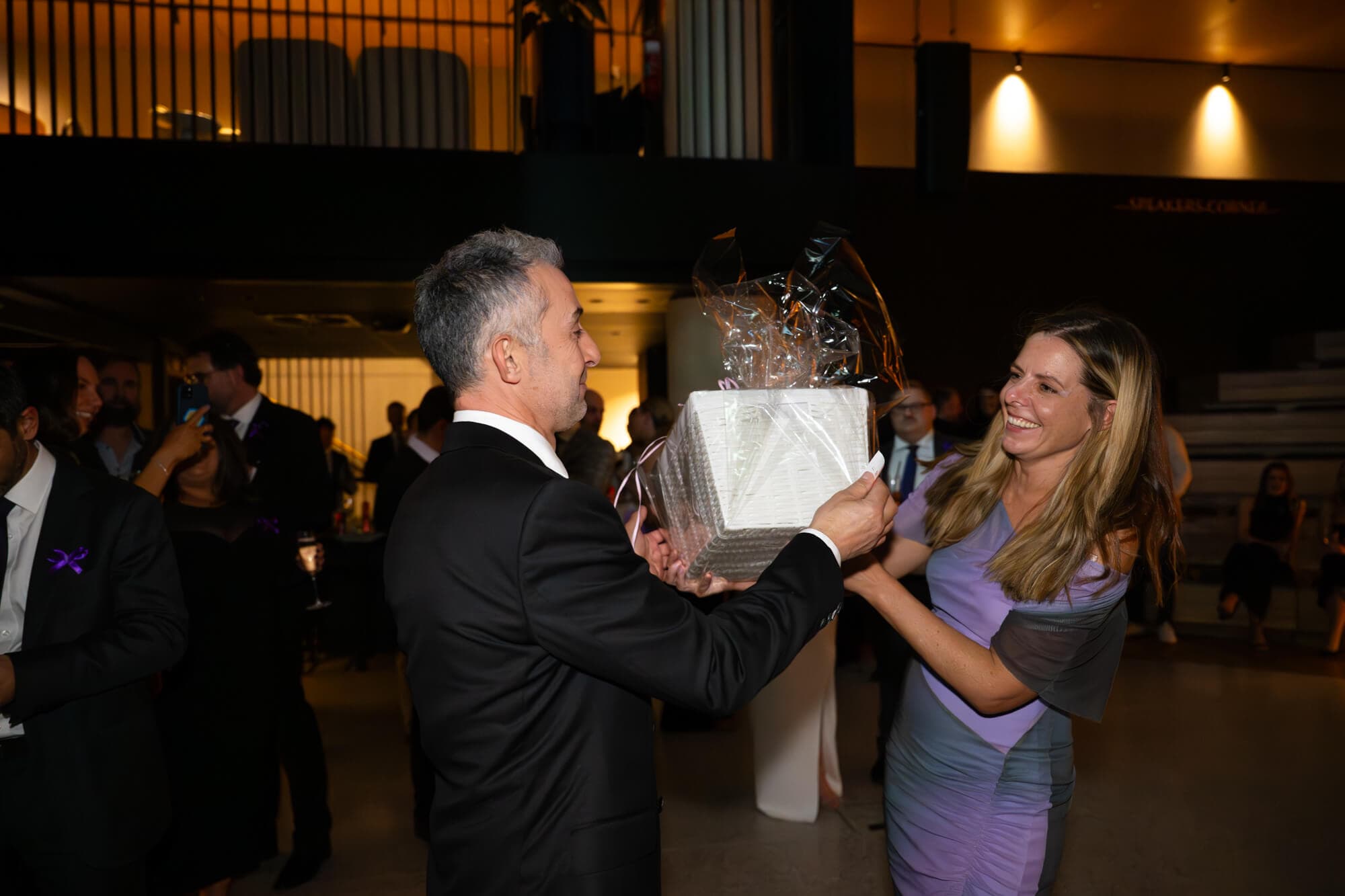 A guest presented with a wrapped hamper prize at the 2025 gala, both laughing