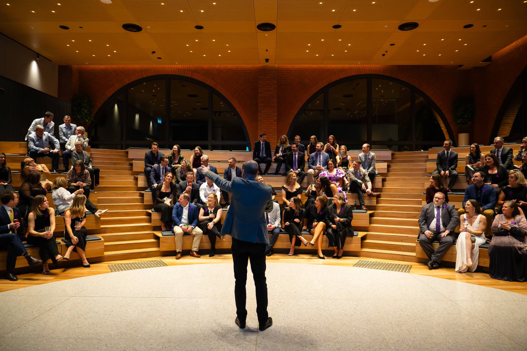 A host addressing the full seated crowd from the centre of the room